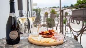 A table with a bottle of Desio Brut wine, two glasses of white wine, and a charcuterie board with cheese, meats, and olives. - Perlage Suite Luxury B&B (Alberobello)