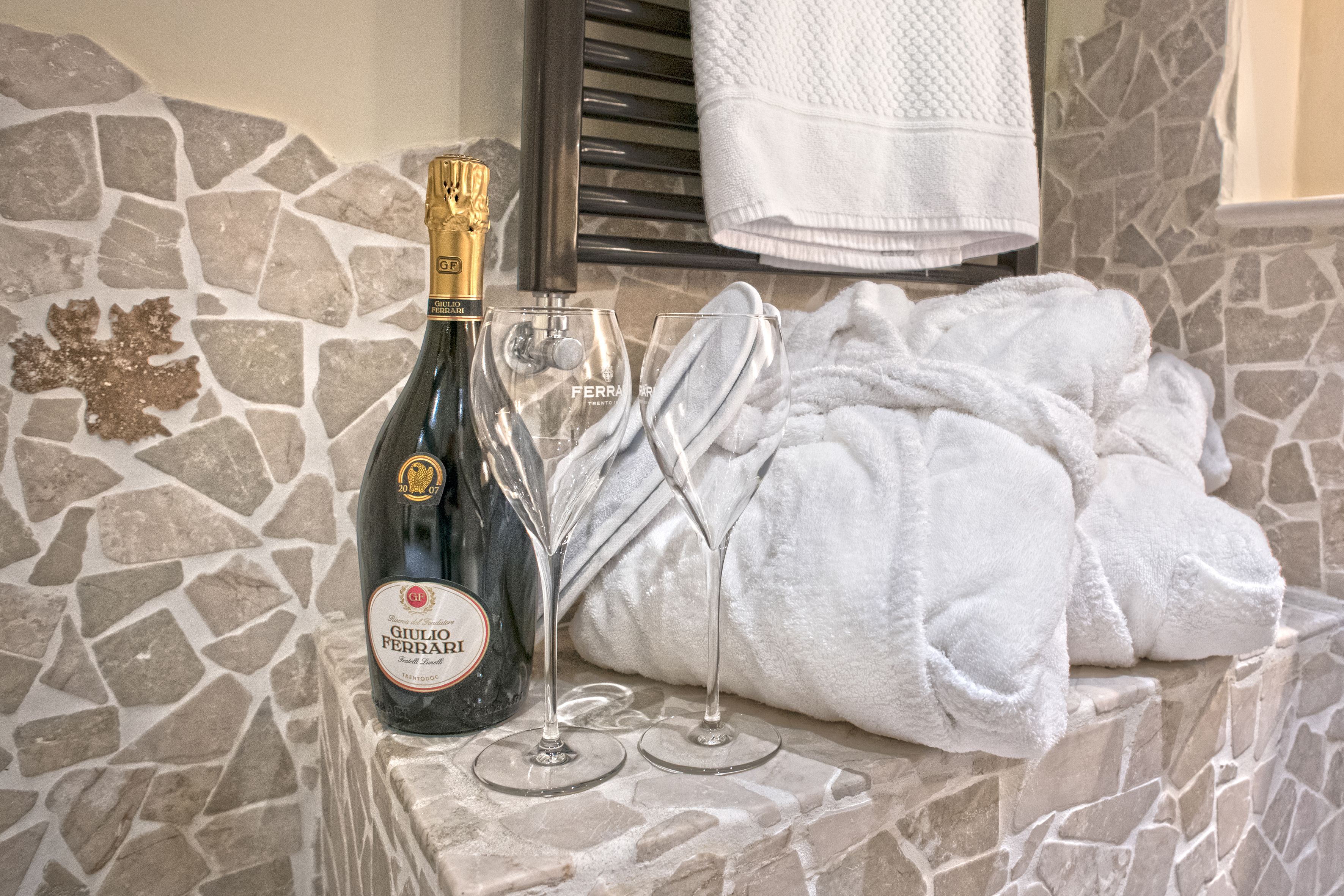 Una botella de vino Giulio Ferrari, dos copas de vino y una toalla blanca sobre una pared de piedra.