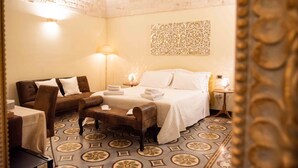 A hotel room with a bed, a sofa, a chair, a table, and a decorative wall piece. - Perlage Suite Luxury B&B (Alberobello)