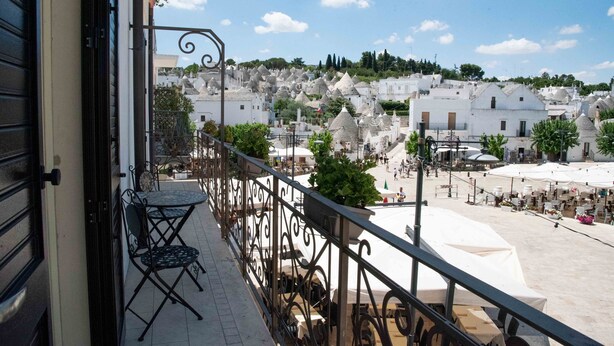 A balcony with a table and chairs, overlooking a town with white buildings and a clear sky. - Perlage Suite Luxury B&B (Alberobello)