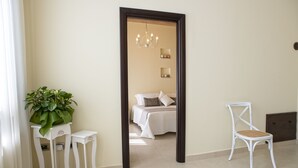 A room with a bed, a white chair, a potted plant, and a mirror reflecting a chandelier. - Perlage Suite Luxury B&B (Alberobello)