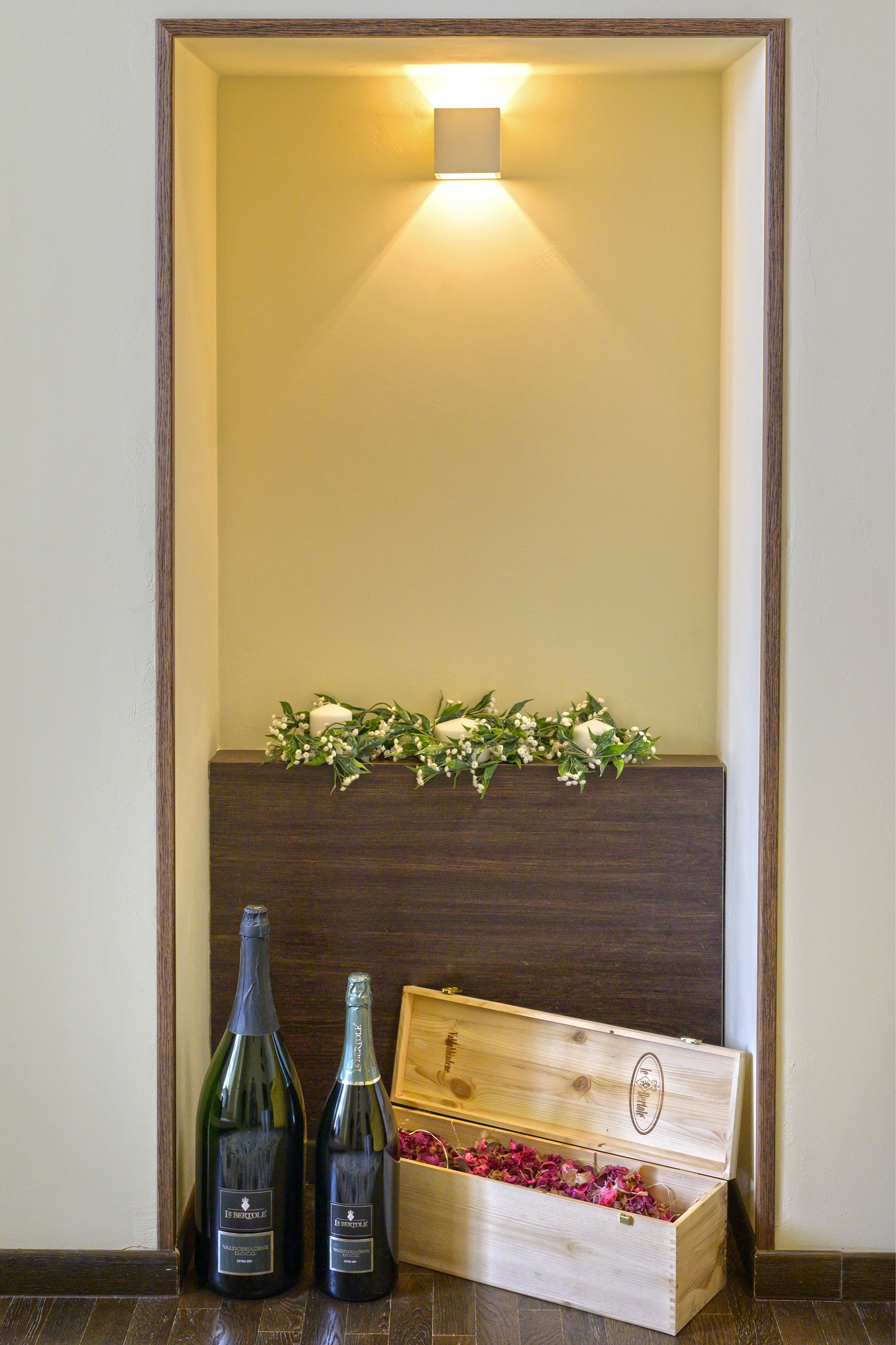 Zwei Weinflaschen und eine Holzkiste mit Blumen an einer Wand.