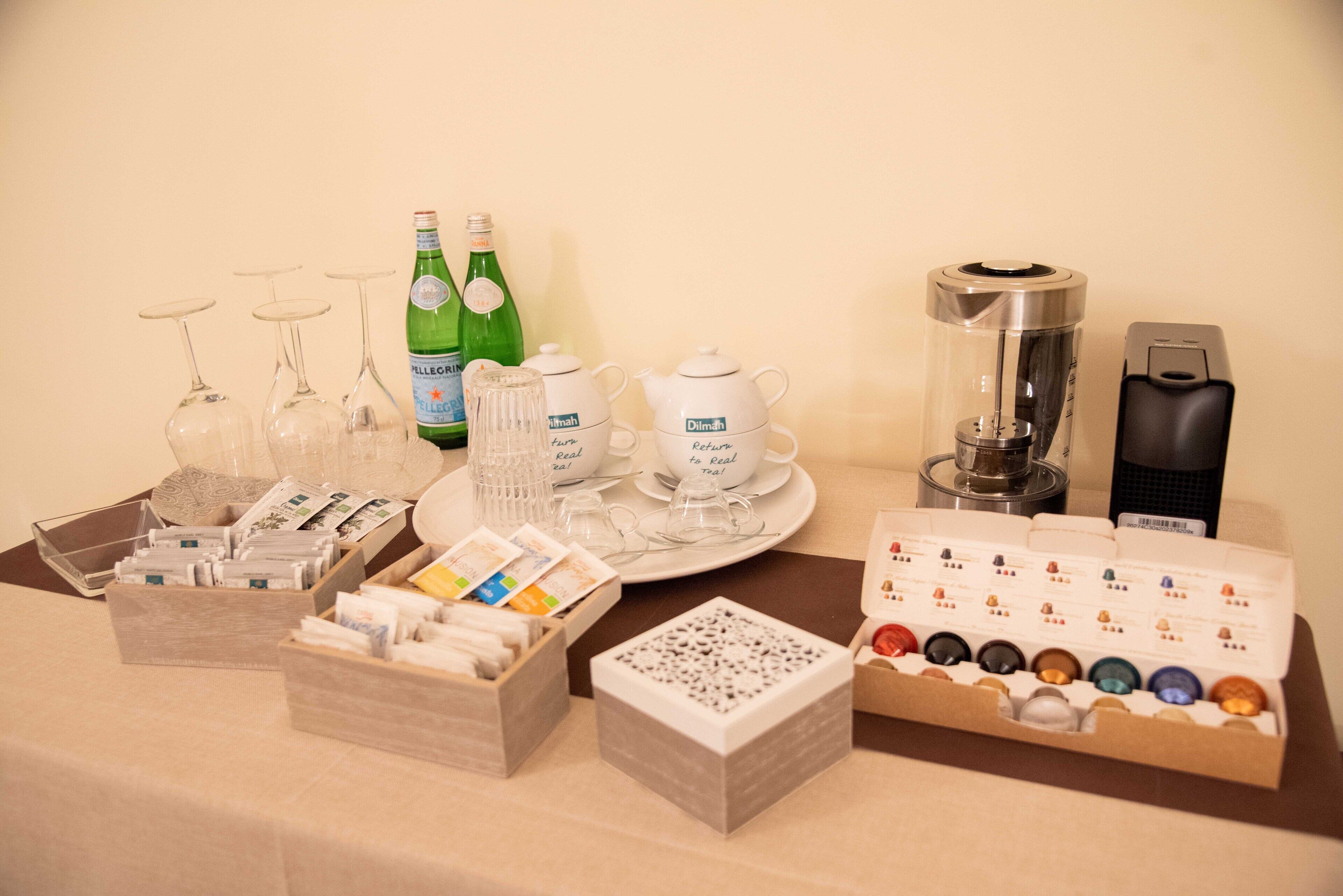 Uma mesa com diversos objetos, incluindo copos de vinho, garrafas, bules e uma máquina de café.