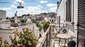 A balcony with a wrought iron railing, a potted plant, and a view of a town with traditional buildings. - Perlage Suite Luxury B&B (Alberobello)