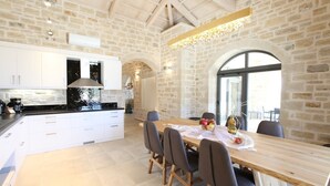 Une cuisine moderne avec des meubles blancs, une table à manger en bois et un mur en pierre en arrière-plan.