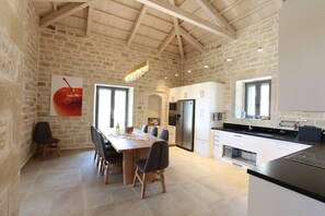 Une cuisine spacieuse avec un grand îlot central, un coin repas avec une table et des chaises en bois, et un mur en pierre.