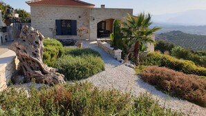 Une maison en pierre avec un toit recouvert de tuiles rouges, un chemin de gravier et une vue sur le paysage.