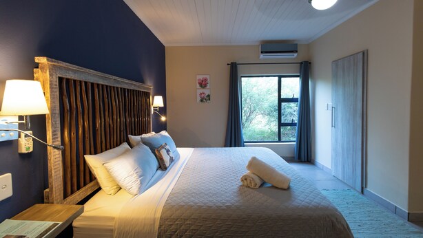 Une chambre d’hôtel avec un grand lit, une tête de lit en bois, une table de chevet avec une lampe et une fenêtre avec des rideaux.