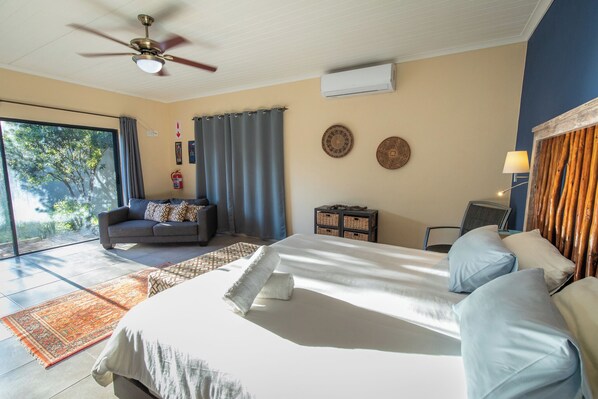 A bedroom with a large bed, a sofa, a ceiling fan, and a view of the outdoors. - Asuite-Dream (Hoedspruit)