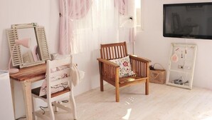 Une pièce avec un bureau en bois, une chaise, un téléviseur et une fenêtre ornée de rideaux légers.