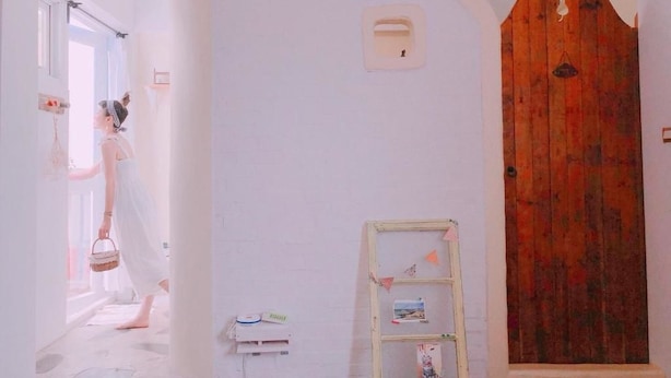 Un couloir avec une porte en bois, un mur blanc orné d’une petite fenêtre et une étagère avec des photos.