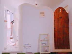 Un passadís amb una porta de fusta, una paret blanca i una finestra petita, i una estant amb fotos.