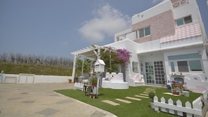 Une maison moderne à deux étages, avec une façade blanche, un patio couvert et un petit jardin.