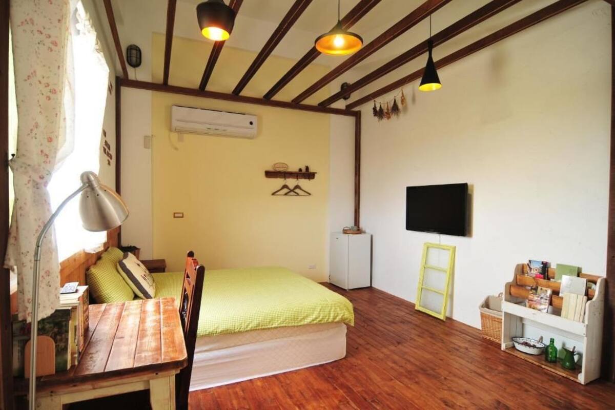 A small, cozy room with a bed, a desk, a lamp, a television, and a shelf with items.