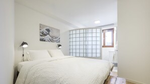 Un dormitorio con cama, dos lámparas de noche, un cuadro en la pared, una ventana con vistas y un banco de madera.