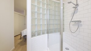 Un baño moderno con ducha de vidrio, paredes de azulejos blancos y suelo de madera.
