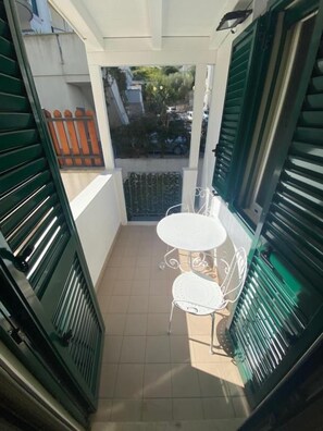 A small outdoor balcony with a white table and chairs, green shutters, and a view of the street. - Casa FioRita (Vieste)