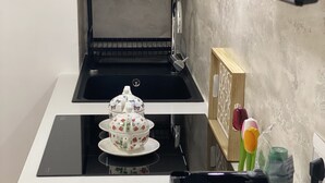 A compact kitchen with a black stove, a white countertop, a black coffee maker, and a decorative teapot on the counter. - Casa FioRita (Vieste)