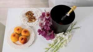 A table with a bottle of champagne, a plate with pastries, and a plate with small round items, possibly fruit or pastries, on a white tablecloth with lace doilies and flowers. - Casa FioRita (Vieste)