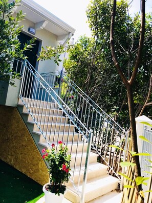 A staircase with metal railings leading to a building entrance, surrounded by greenery and potted plants. - Casa FioRita (Vieste)