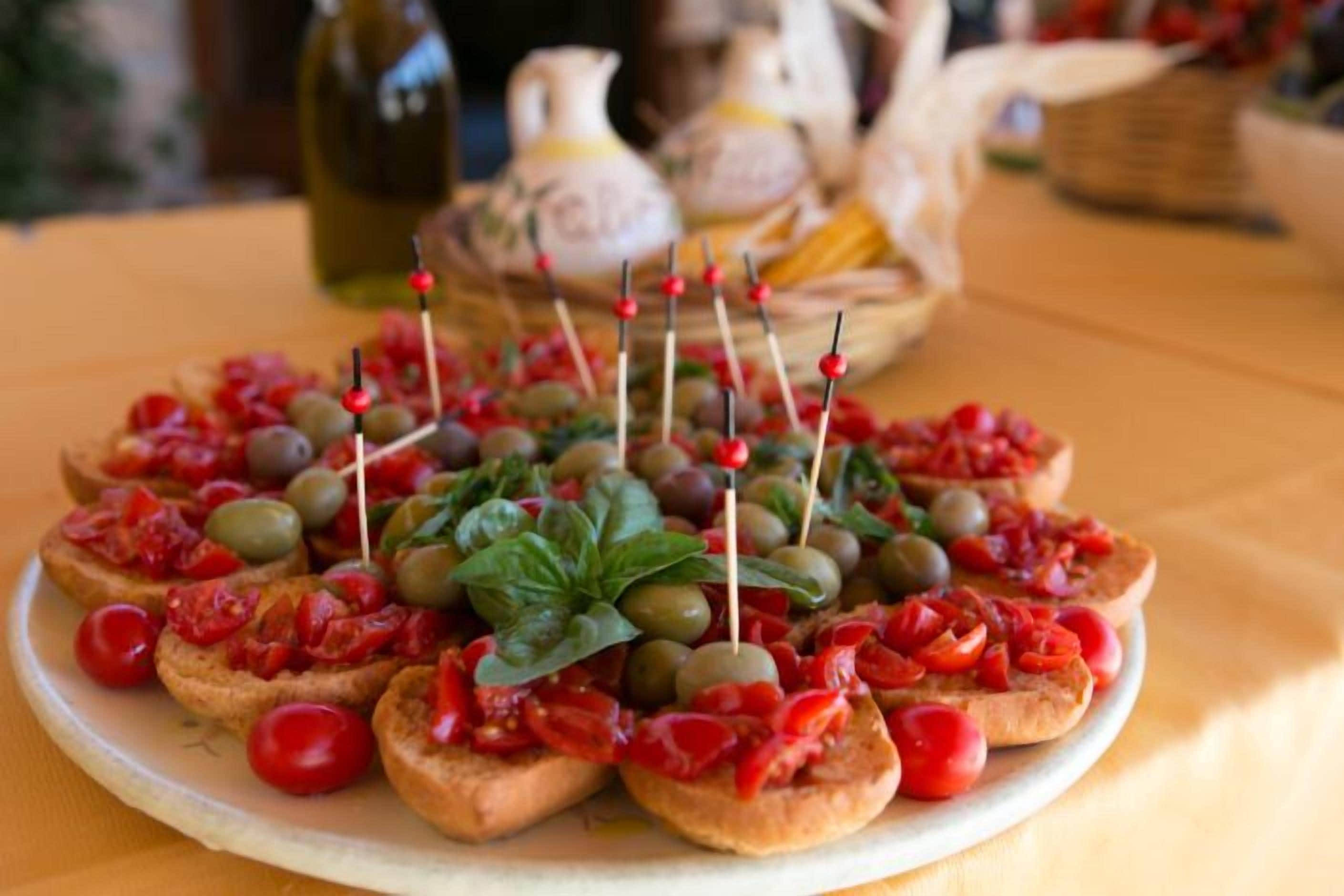 A plate of appetizers with olives, cherry tomatoes, and basil on breadsticks.