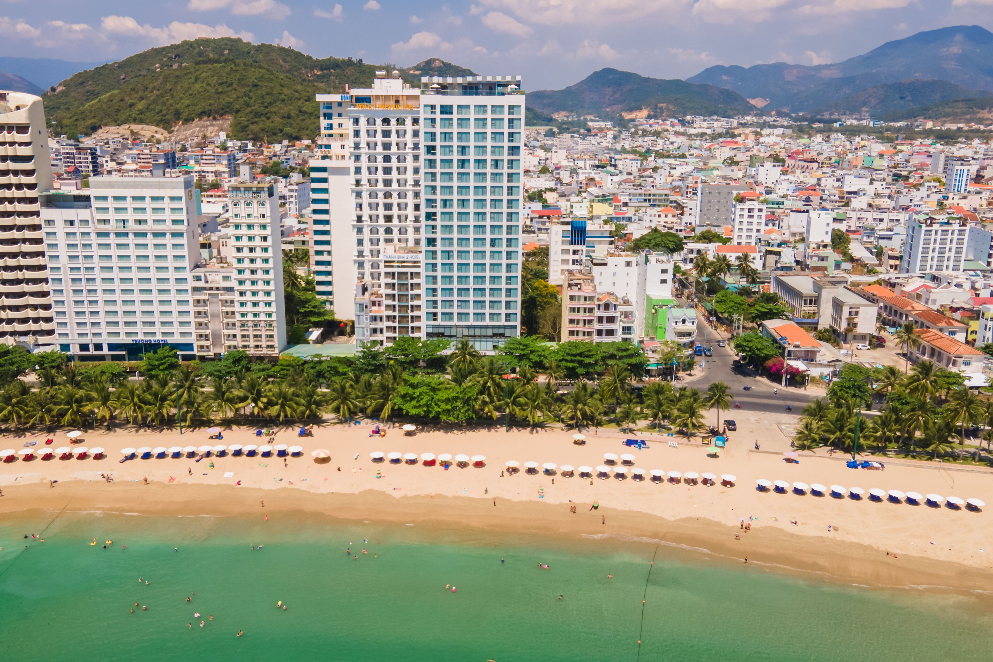 A coastal cityscape with high-rise buildings, a beach with umbrellas, and palm trees.