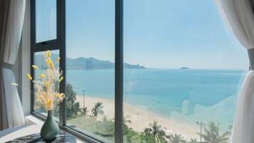 A room with a large window overlooking a beach, a vase with yellow flowers, and a book on a table.
