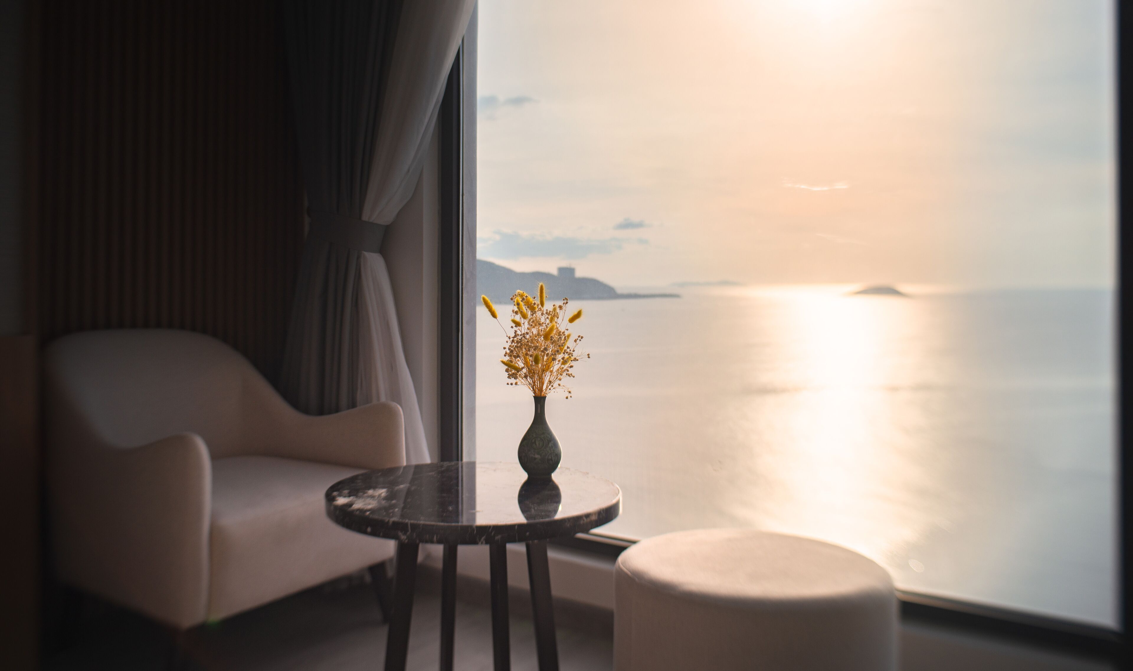 Una habitación con vista al mar, un jarrón con flores secas sobre una mesa y un sofá.