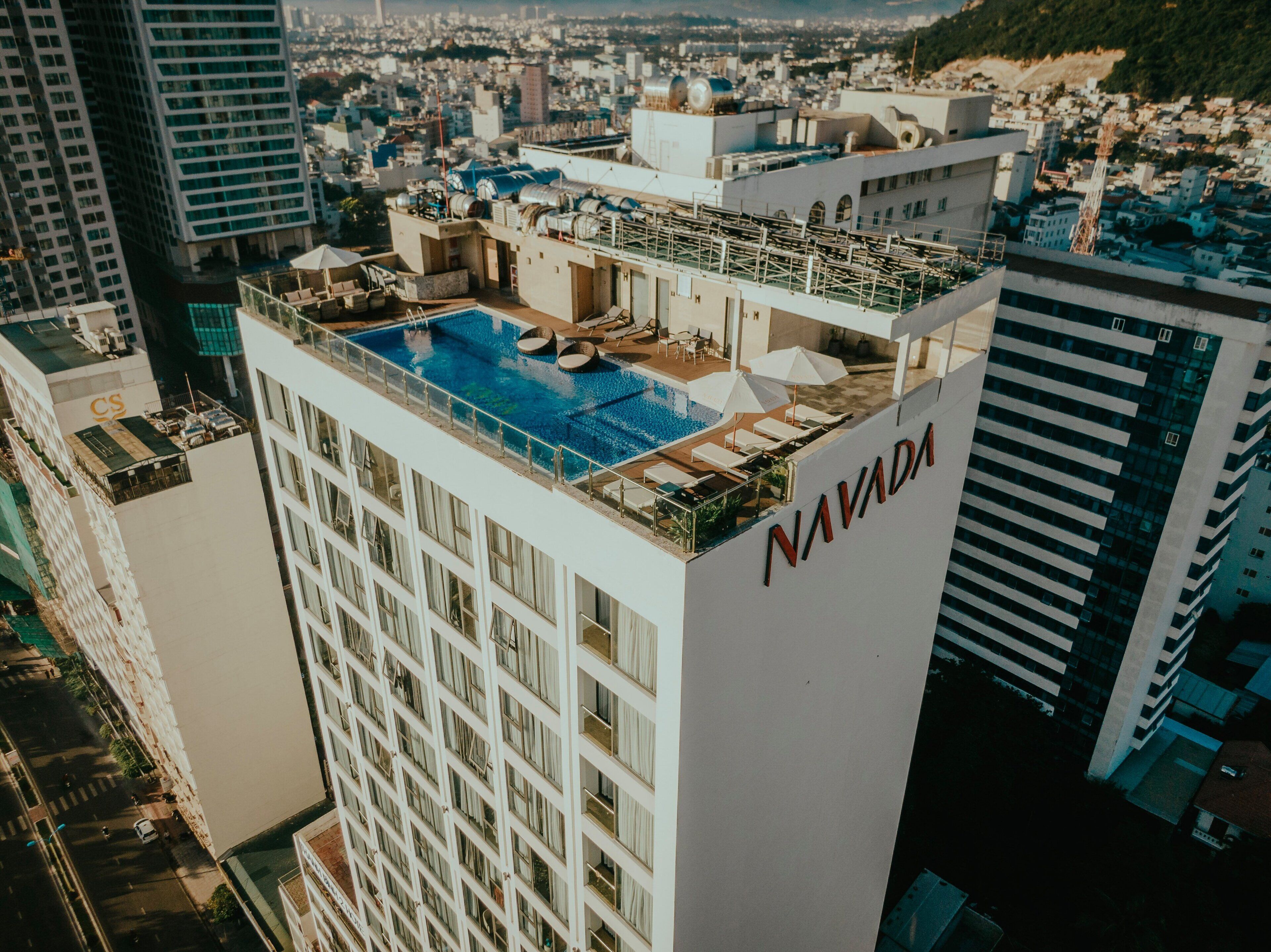 A high-rise hotel with a rooftop pool, multiple balconies, and a view of the cityscape.