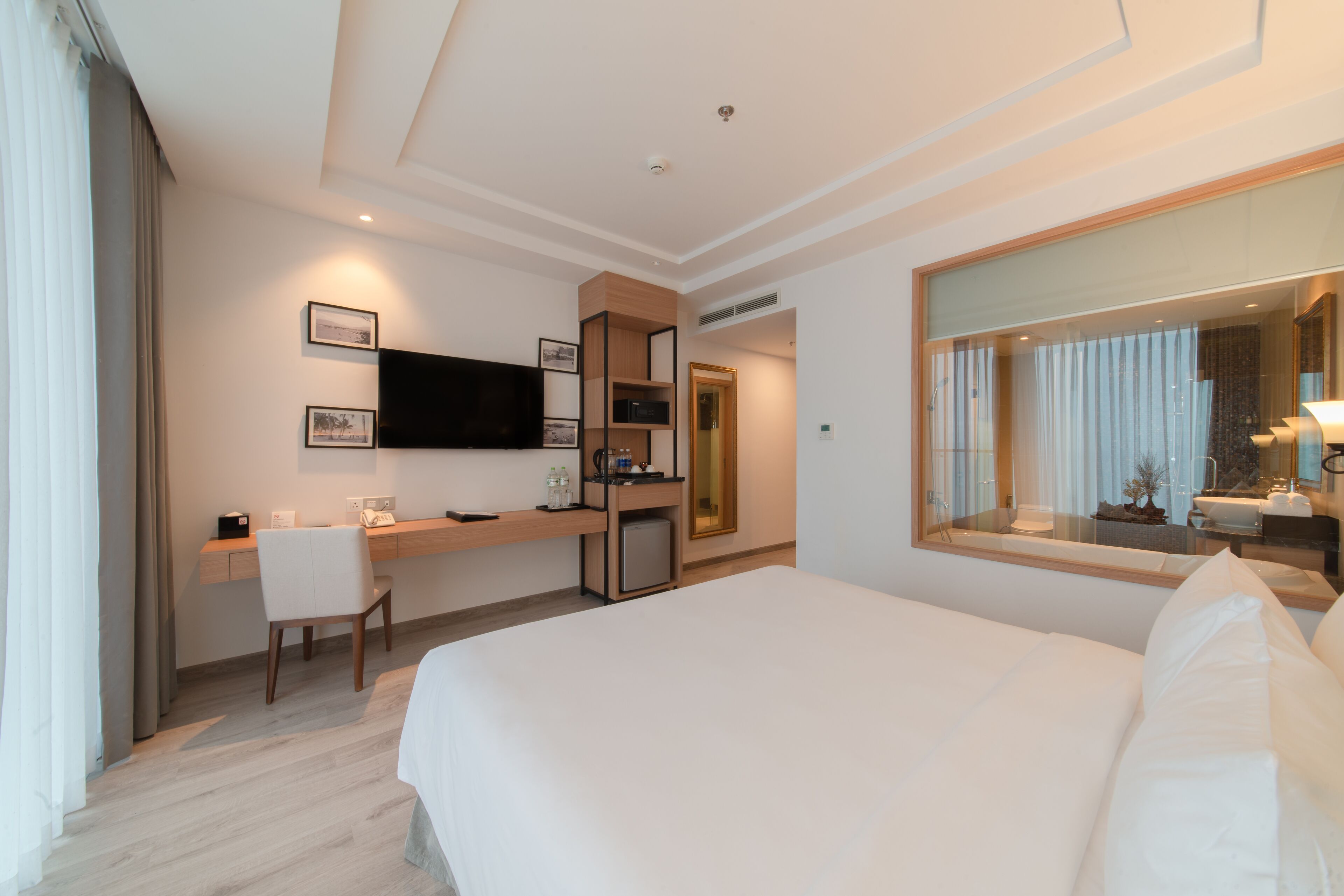 A hotel room with a large bed, a desk with a chair, a television, and a mirror.