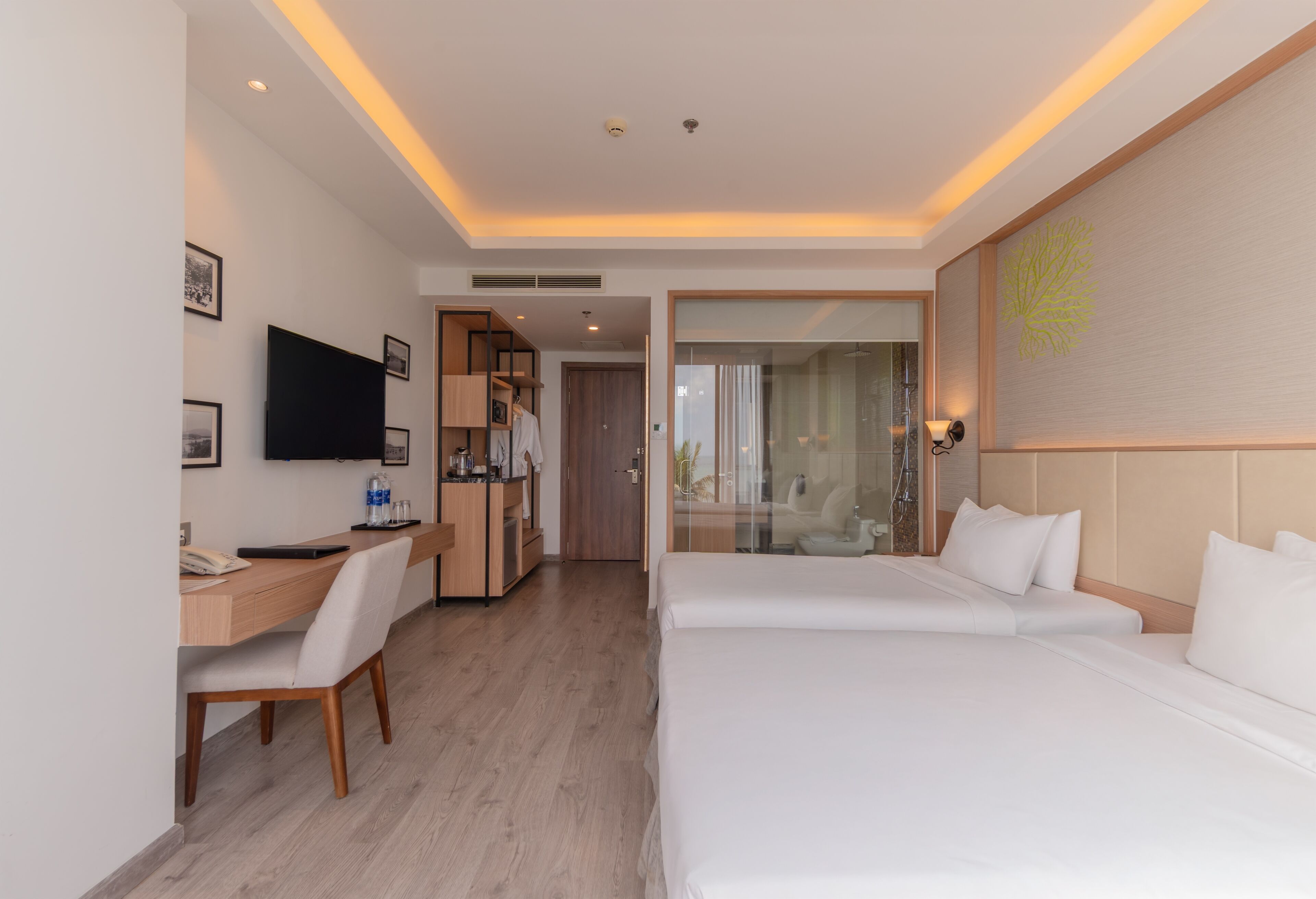 Una habitación de hotel moderna con un escritorio de madera, un televisor de pantalla plana, una cama con ropa blanca y una zona de ducha de vidrio.