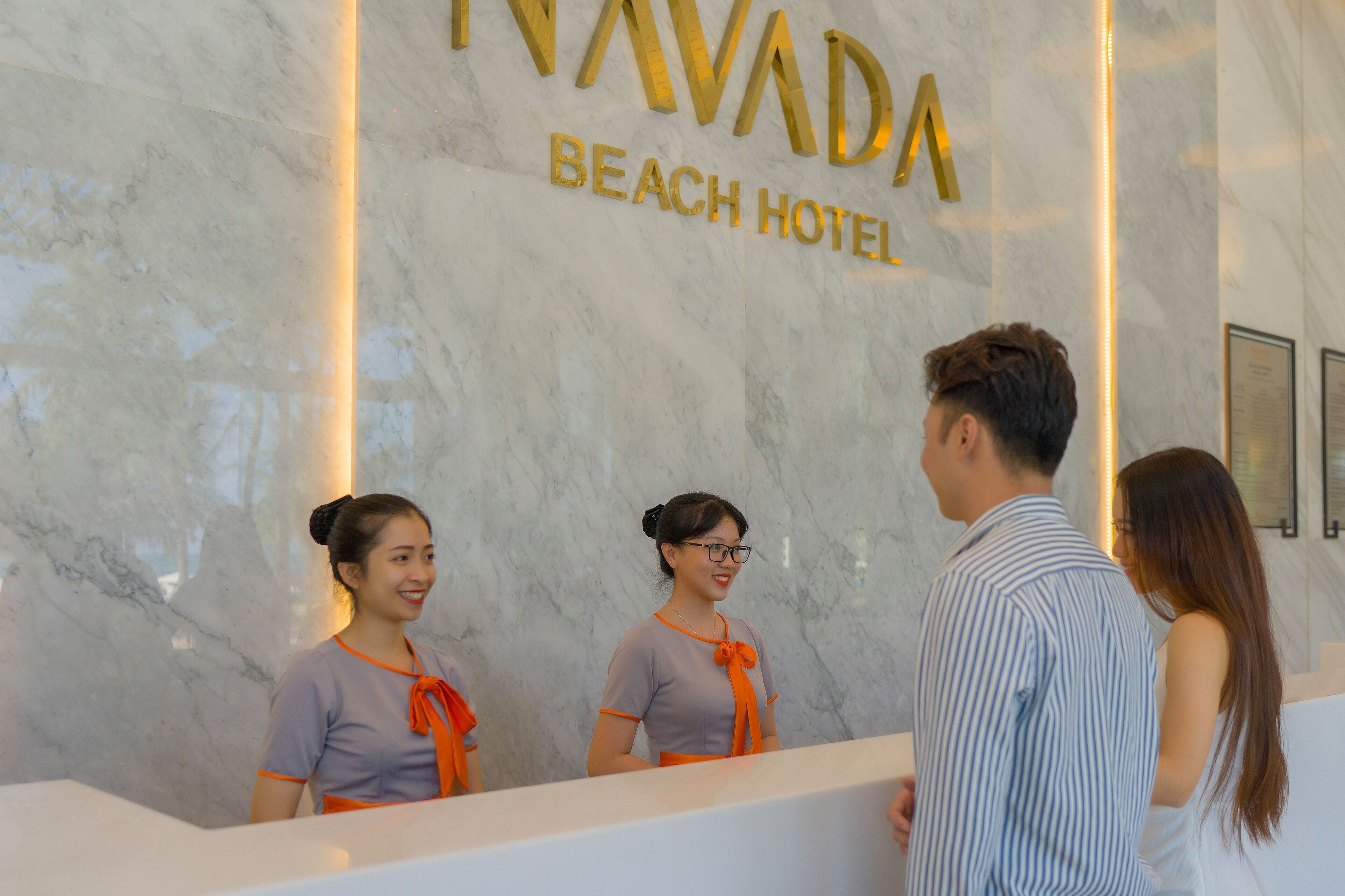 A reception desk at the "NAVADA BEACH HOTEL" with marble walls and a modern design.