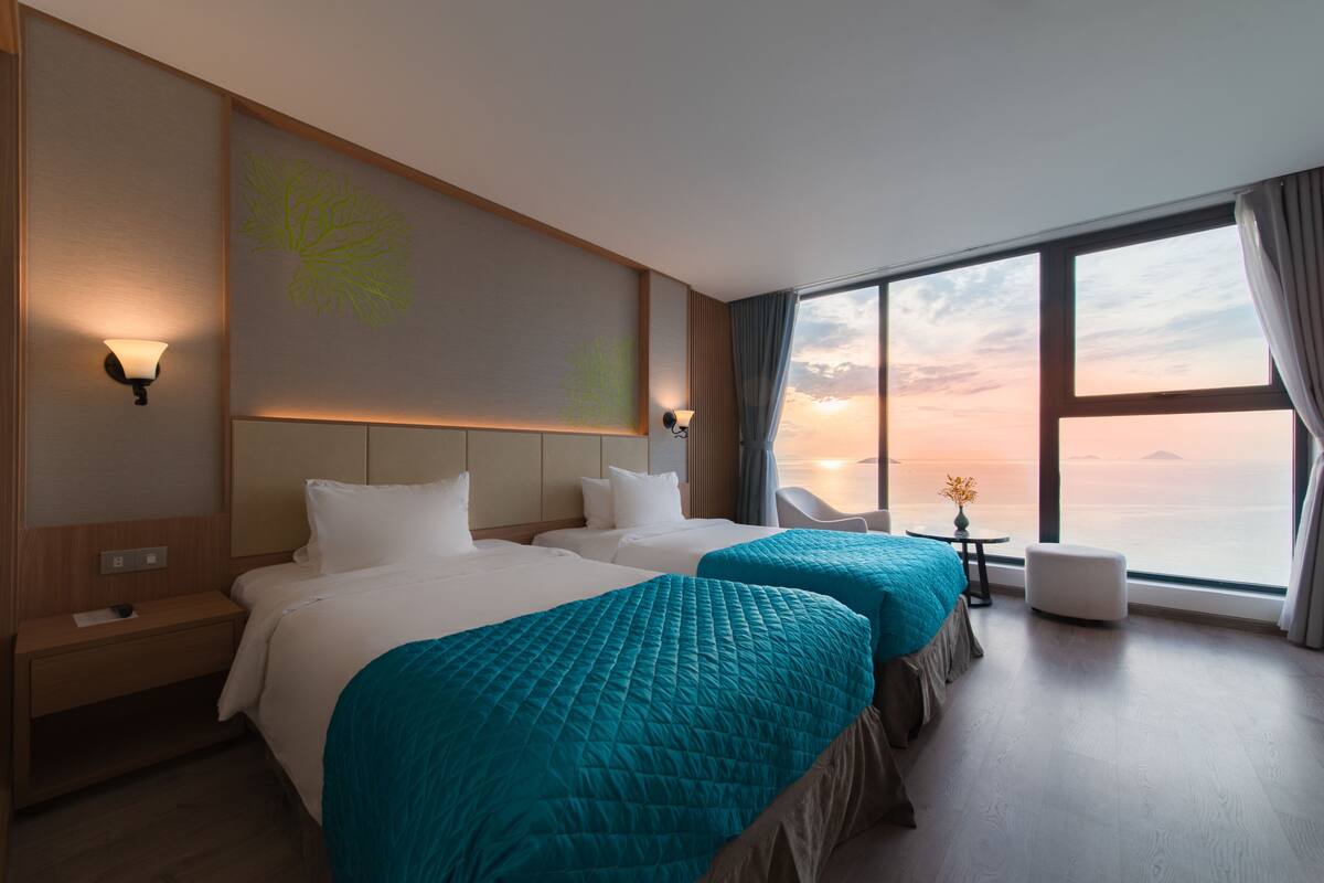 A hotel room with two beds, a large window with a view, and a wall-mounted light fixture.