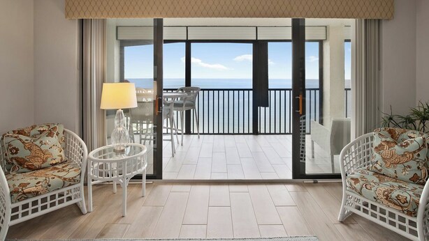 A balcony with a view of the sea, furnished with two white chairs and a table, and a lamp. - Vanderbilt Gulfside on Vanderbilt Beach (Naples)