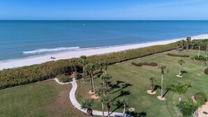 An aerial view of a coastal property with a beach, a well-maintained lawn, and a pathway leading to the beach. - Vanderbilt Gulfside on Vanderbilt Beach (Naples)