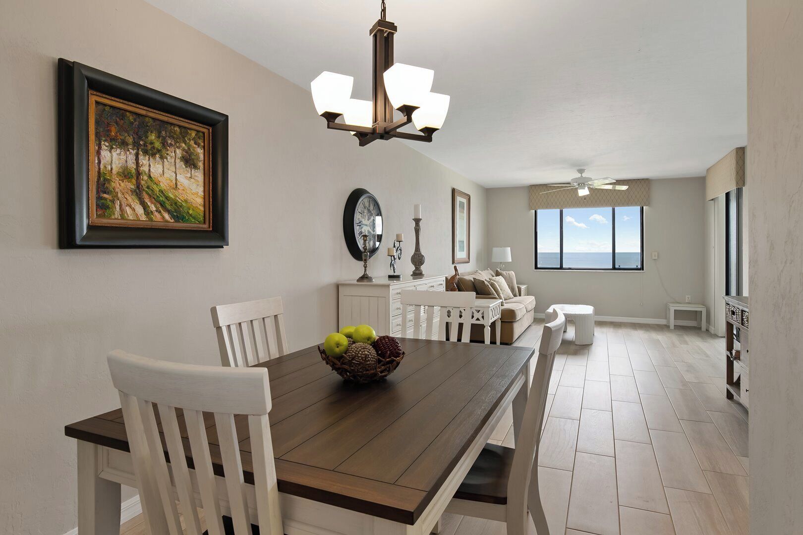 A dining area with a wooden table, white chairs, a chandelier, and a painting on the wall.