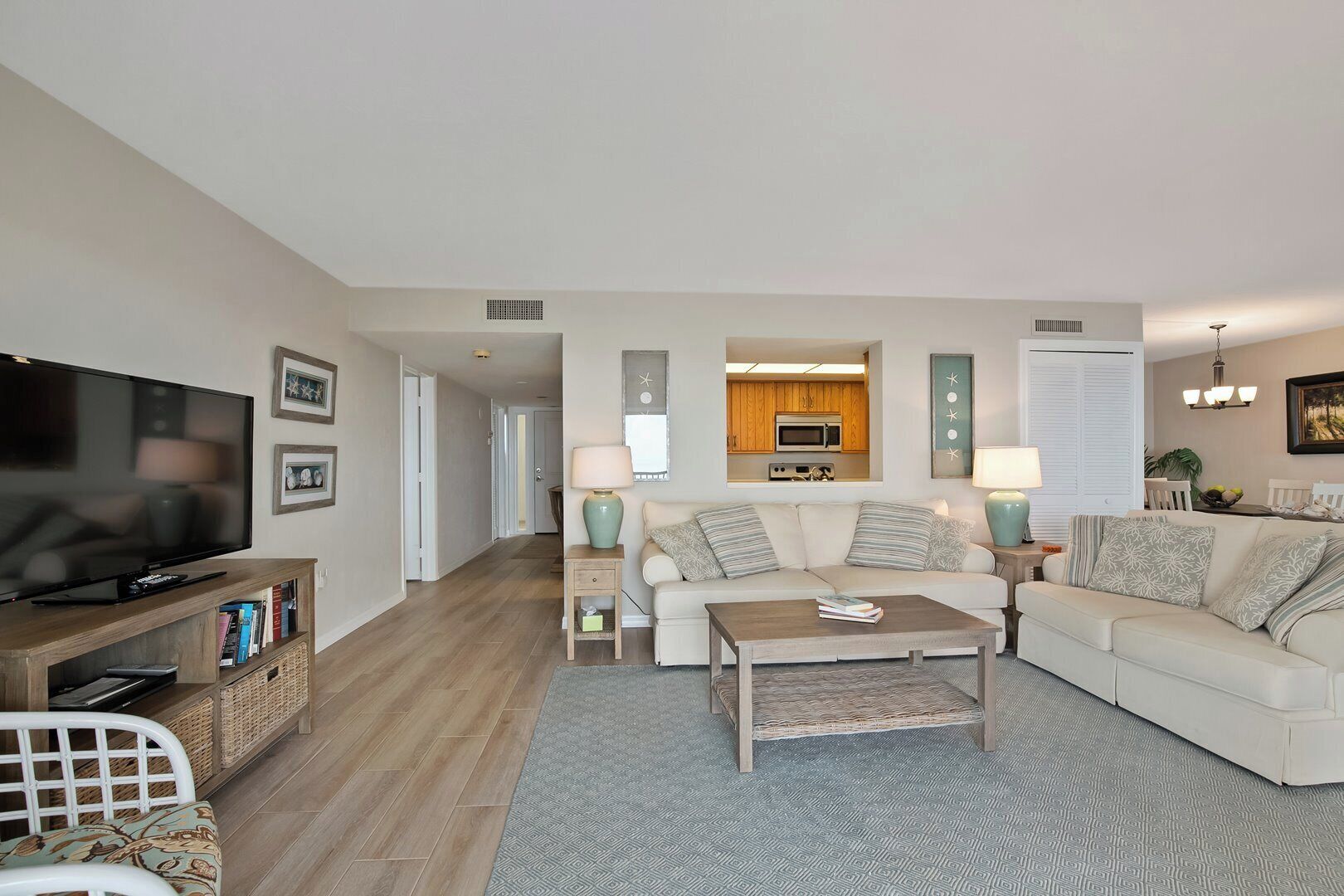 A living room with a television, sofa, coffee table, and a kitchen area visible through an open door.