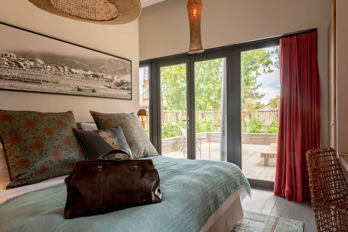 A bedroom with a bed, pillows, a suitcase, a television, and a window with curtains.
