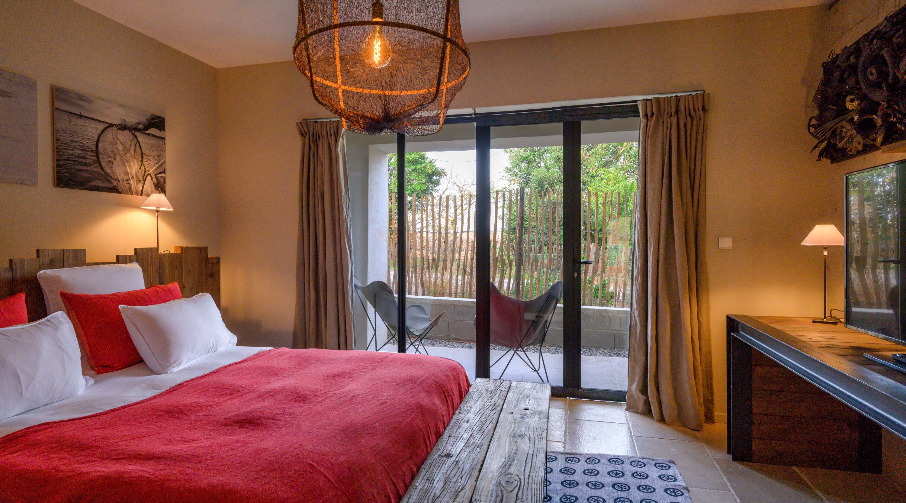 Un dormitorio con una cama grande, un escritorio, una silla y vistas a un jardín a través de una puerta corredera.