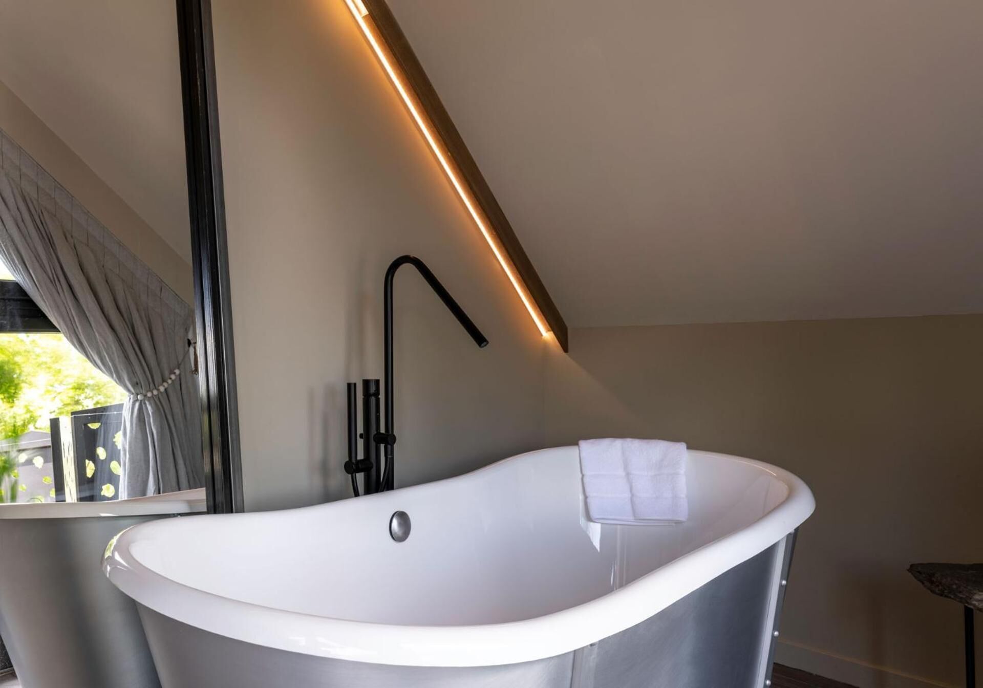 Une salle de bain moderne avec une baignoire sur pieds, un robinet noir élégant et une longue bande lumineuse placée au-dessus de la baignoire.