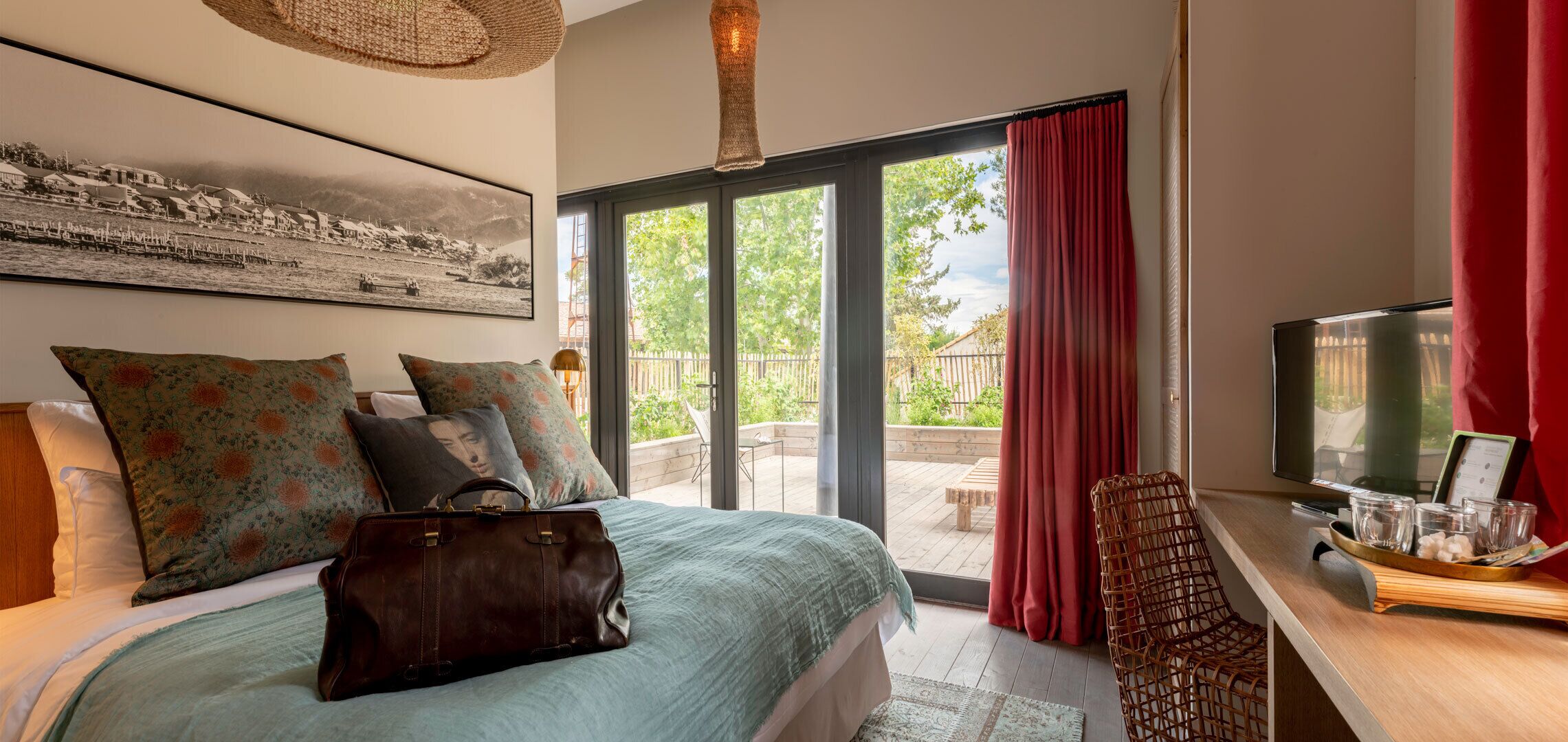 Un dormitorio con cama, almohadas, una maleta, un televisor y una ventana con cortinas.