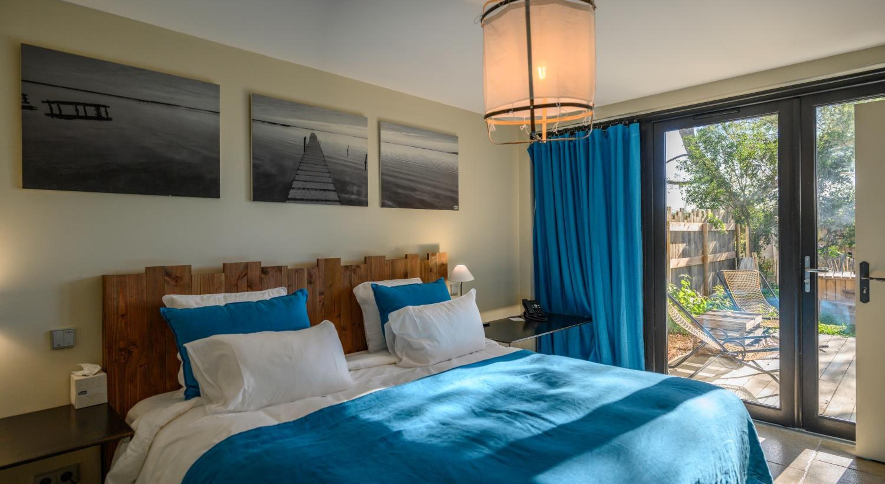 Une chambre à coucher avec un grand lit, une tête de lit en bois et une vue sur un jardin, accessible par une porte-fenêtre coulissante.