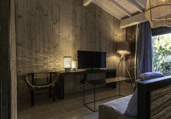 Una habitación con pared de madera, televisor sobre un mueble bajo, una silla, un sofá y una lámpara.