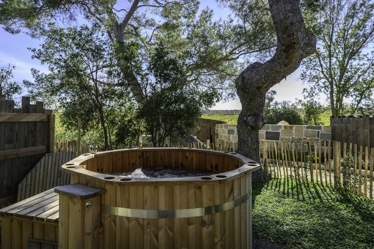 A wooden hot tub in a backyard with a wooden fence and trees.