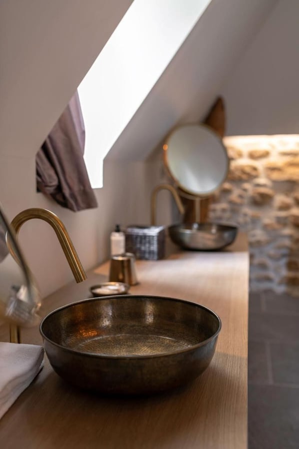Un baño con diseño moderno, que incluye un espejo grande, un lavabo con cuenco y una pared de piedra al fondo.