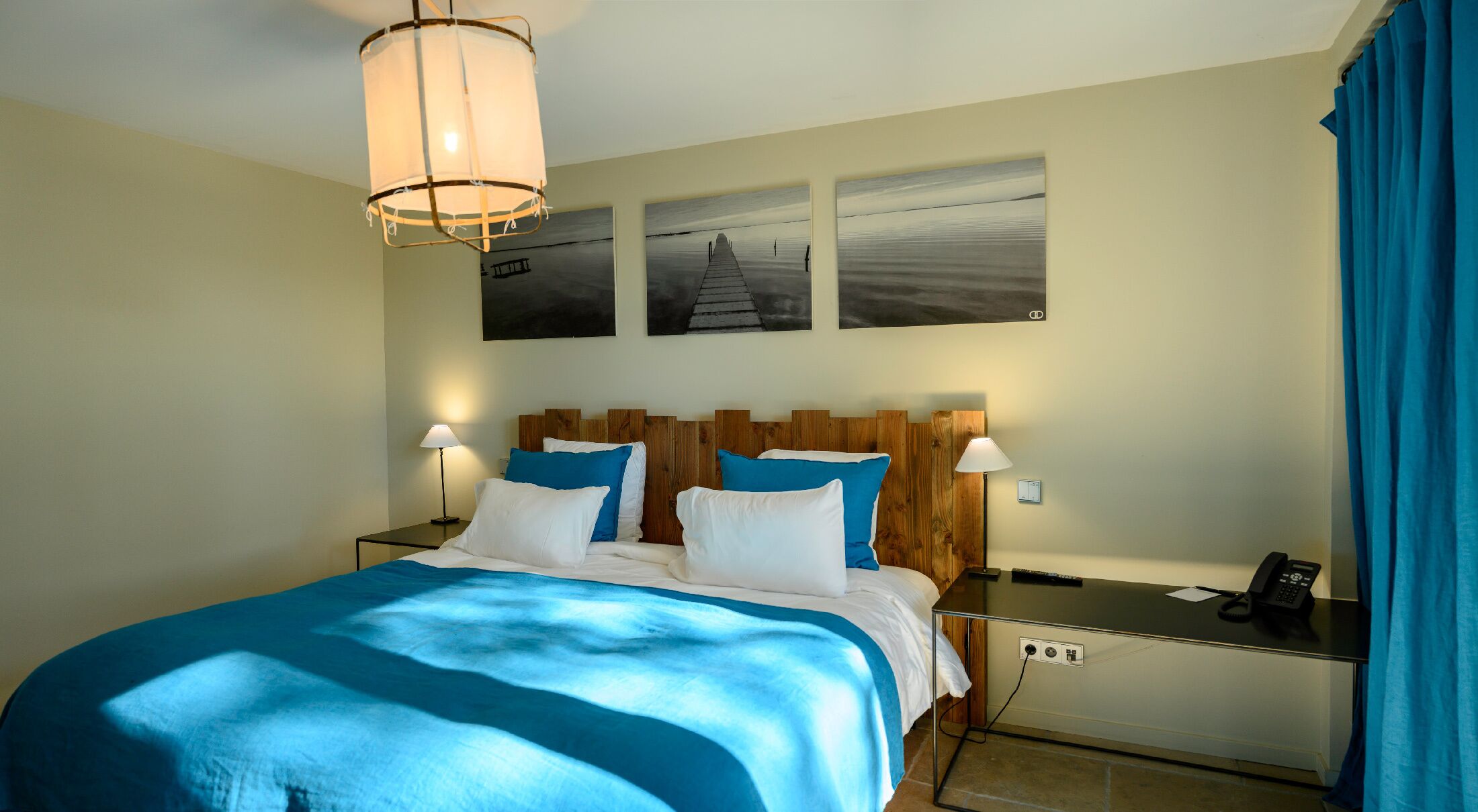 Habitación de hotel con una cama, mesitas de noche, lámpara, teléfono y obras de arte en la pared.