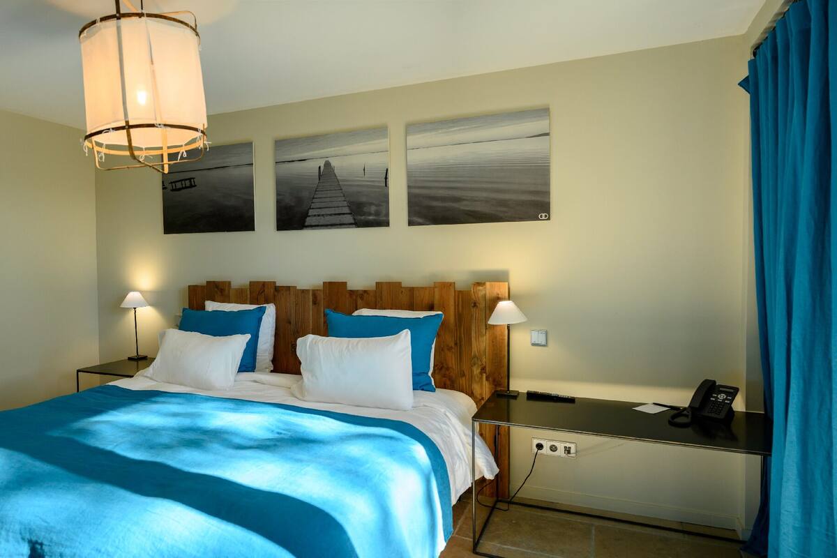 A hotel room with a bed, bedside tables, a lamp, a phone, and artwork on the wall.