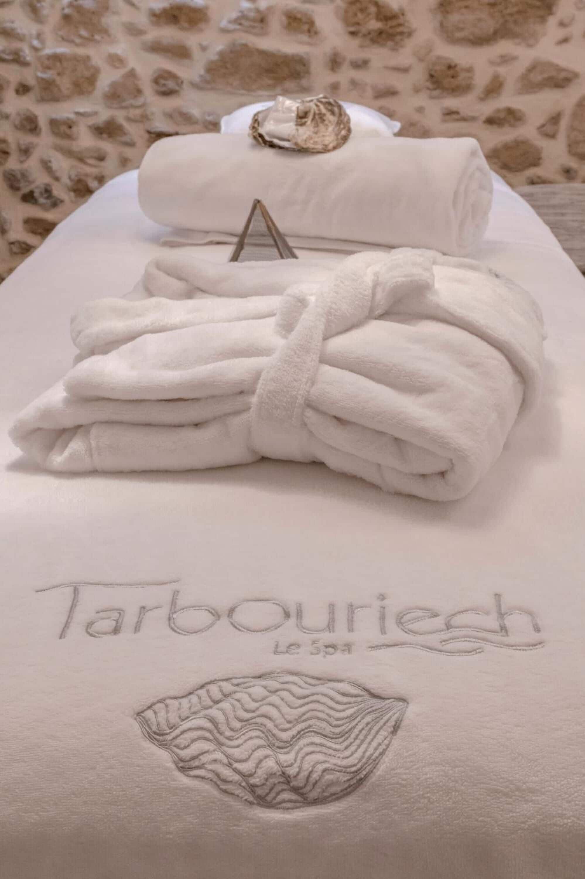 A spa bed with folded towels and a towel rack, featuring the inscription "Tarbouriech Le Spa" and a shell design.