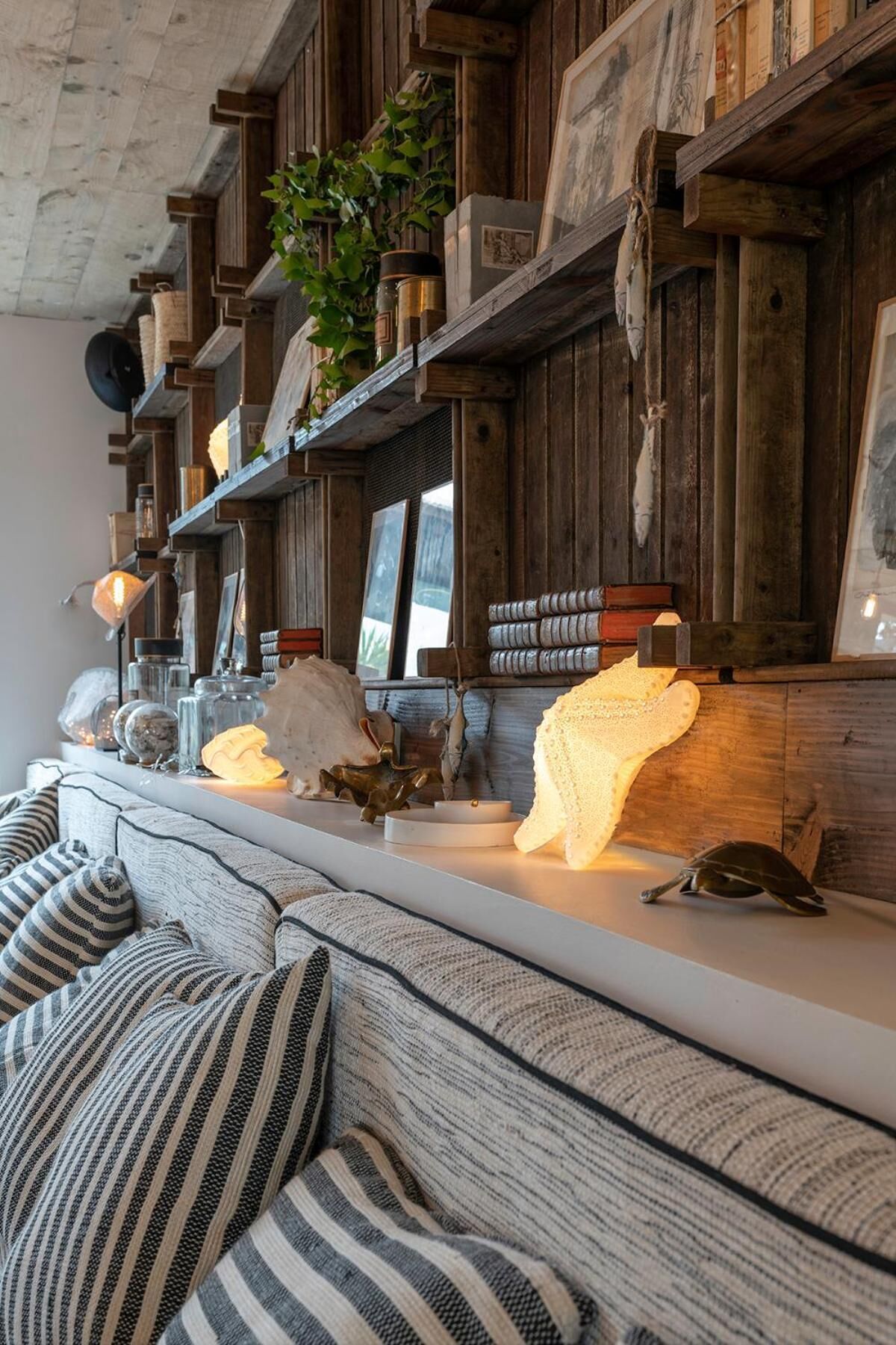 Una sala de estar acogedora con un muro de madera, estantes con adornos, un sofá con cojines a rayas y una ventana con vistas.