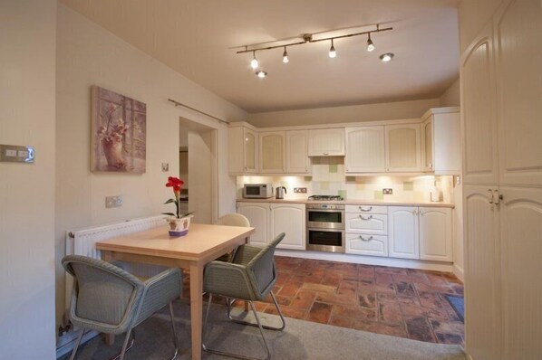 A compact kitchen with white cabinets, a dining table with two chairs, and a radiator on the wall.